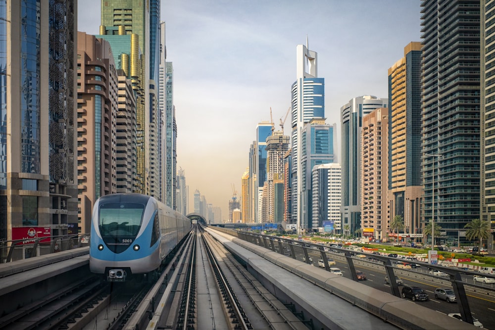 white and blue train on rail road near city buildings during daytime