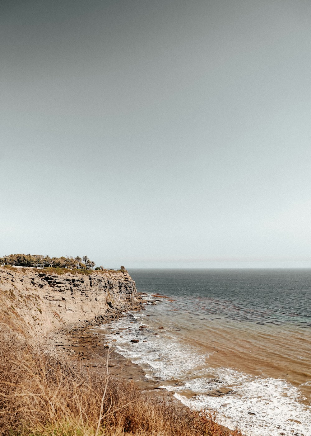 brown rocky mountain beside sea under blue sky during daytime