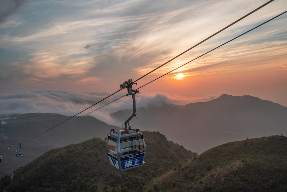 blue and white cable car over green mountains during daytime