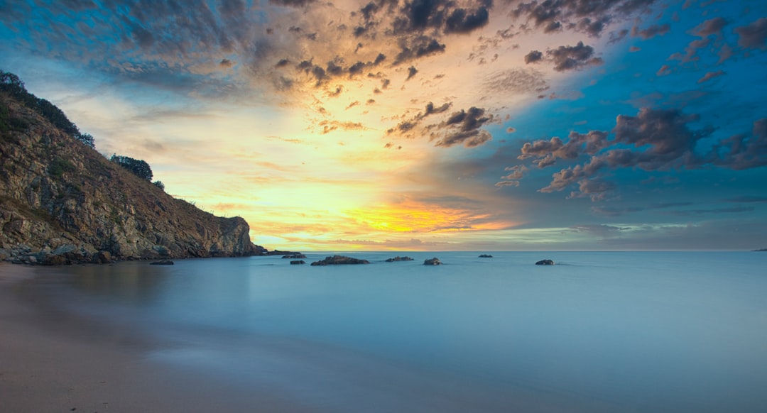 brown and green rock formation on sea under blue sky during daytime