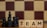 Wooden blocks with the word 'TEAM' are placed next to black chess pieces, including pawns and a king. The background features a blurred chessboard pattern with alternating light and dark squares.