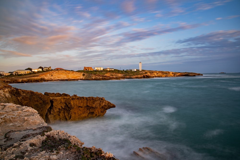 white lighthouse on brown rock formation near body of water during daytime