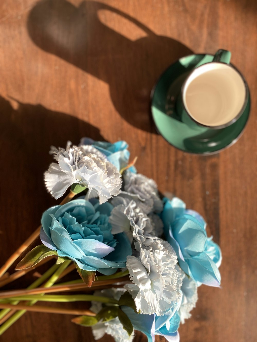 bouquet de fleurs bleues et blanches à côté d’une tasse en céramique verte sur une table en bois marron