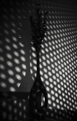 A tall, slender black ceramic vase with an industrial matte finish standing against a white backdrop.