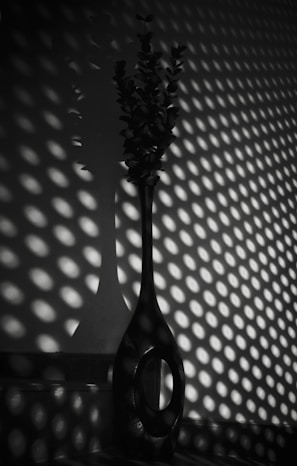 A sleek, tall vase balancing form and volume on a monochrome console table in a softly lit room.
