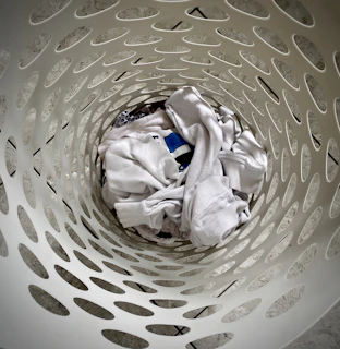 Close-up of a hand holding a lavender-scented breezy clean laundry detergent sheet over a white laundry basket filled with fresh clothes.