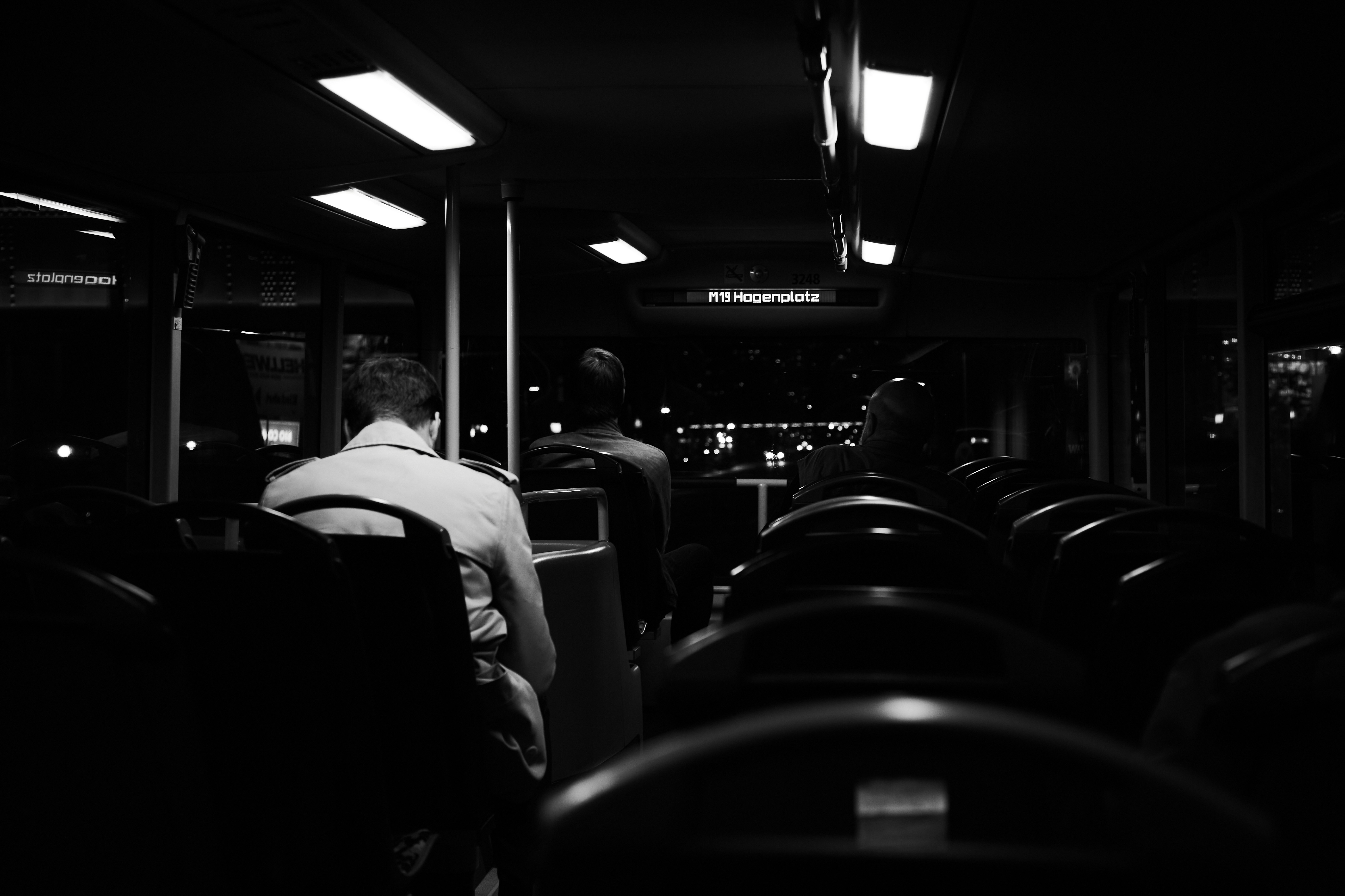 grayscale photo of people sitting on chair, A man sitting alone in the bus seat during an evening ride.