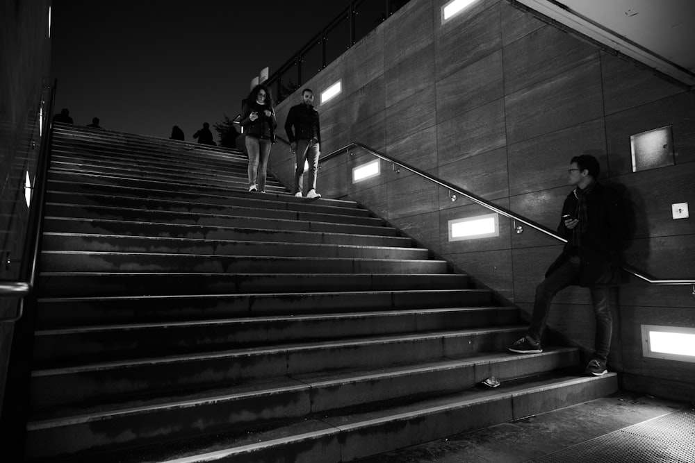 Foto en escala de grises de un hombre con camiseta negra y pantalones caminando por las escaleras