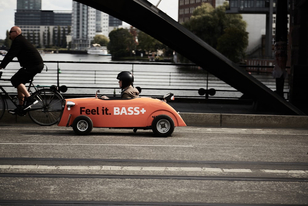 man in black jacket riding orange and black sports car on gray concrete road during daytime