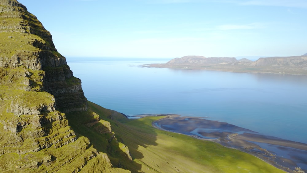 green grass covered mountain beside blue sea under blue sky during daytime