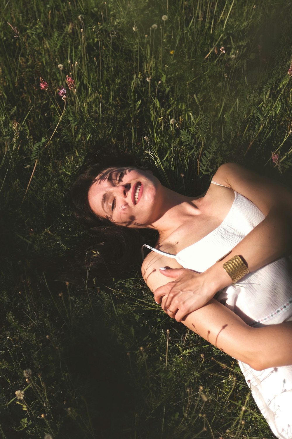 woman in white spaghetti strap top lying on green grass field