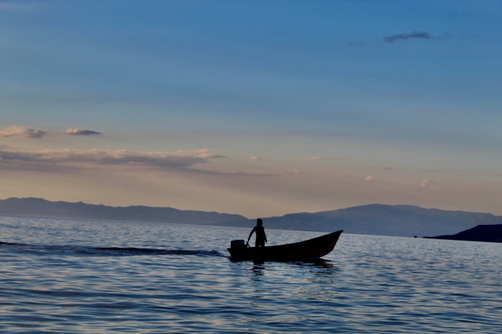 silhouette of man riding on boat during sunset