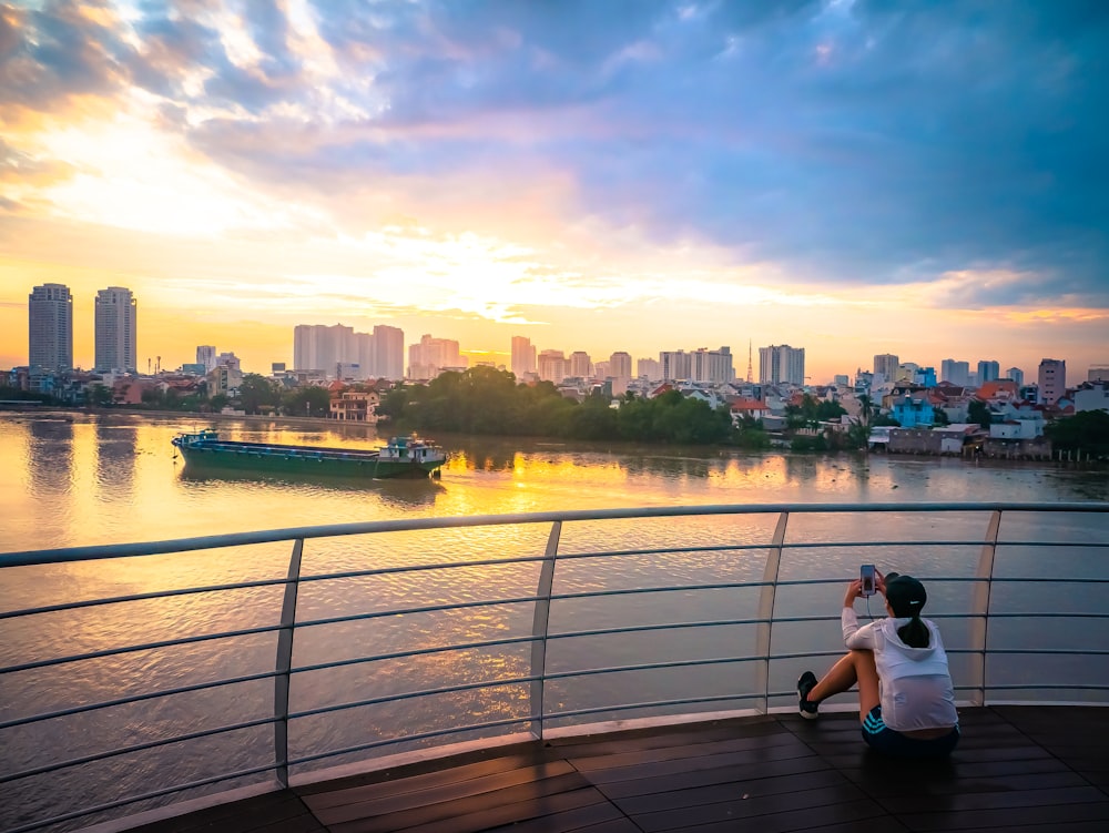 man in white t-shirt sitting on brown wooden dock during daytime