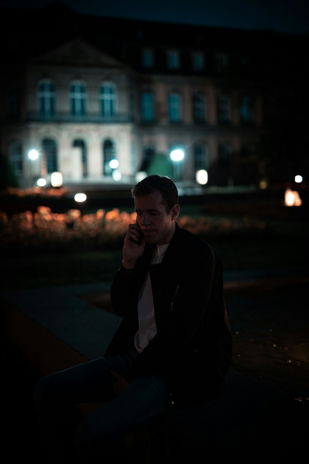 man in black blazer sitting on sidewalk during night time
