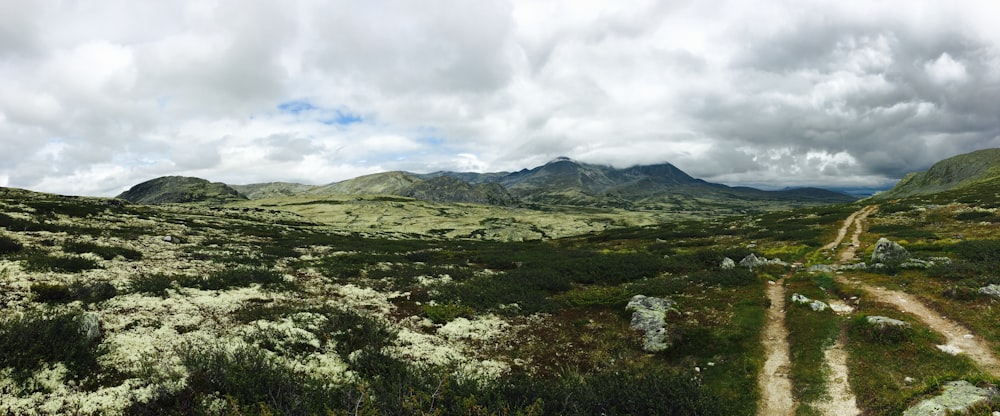 green grass field near mountain under white clouds during daytime