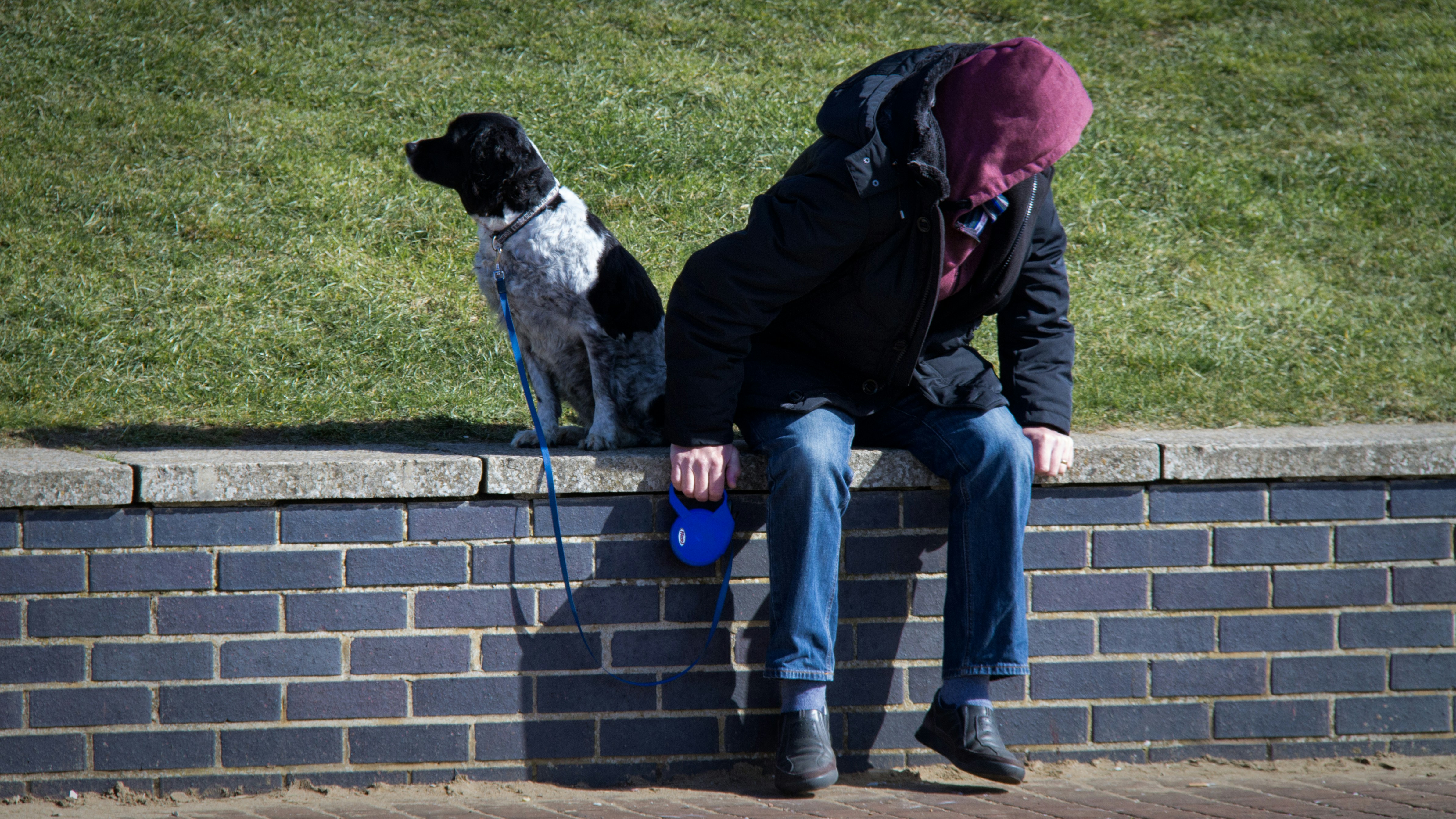 man in black jacket and blue denim jeans sitting on gray concrete bench beside black and