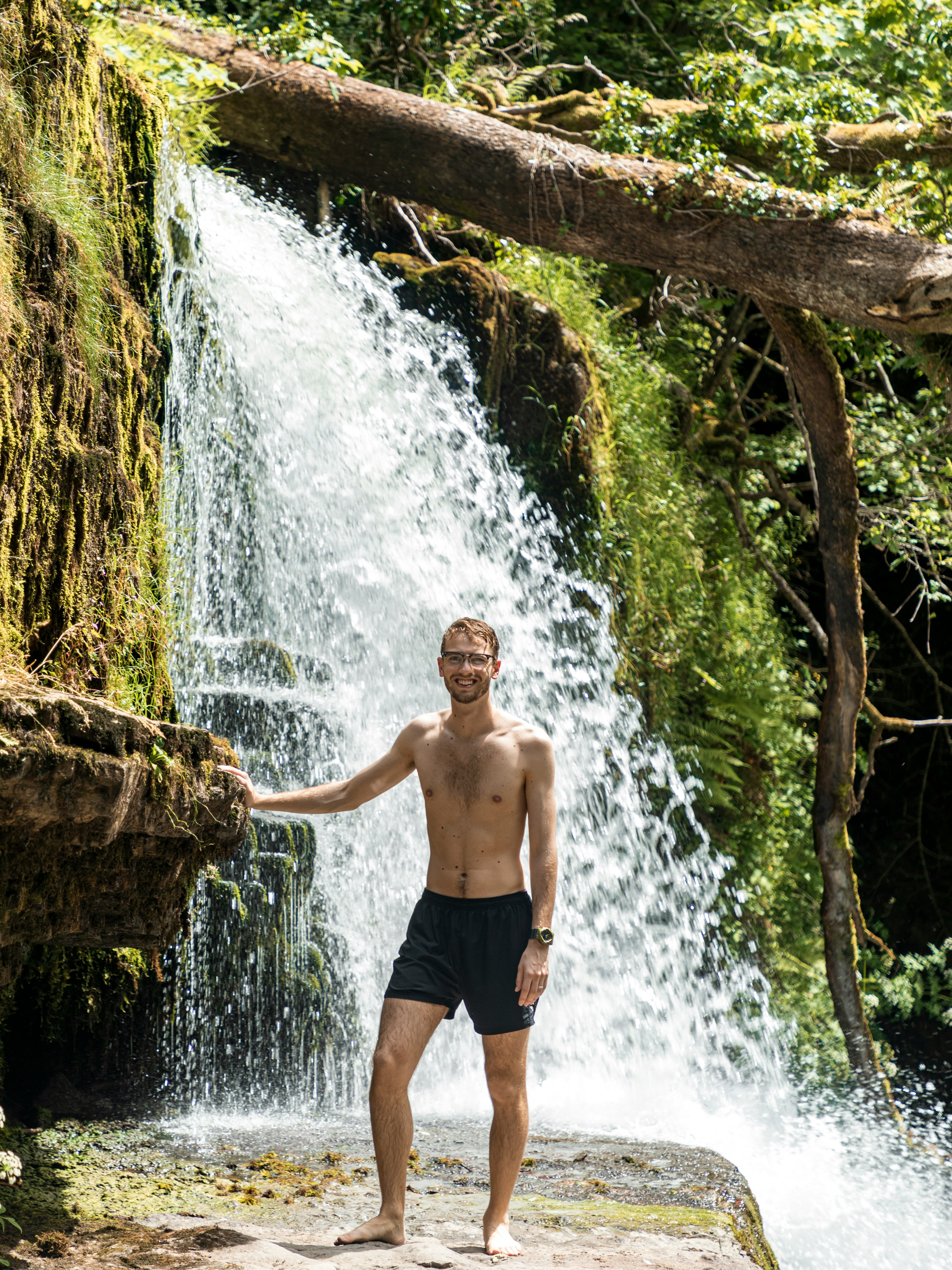 man in blue shorts standing on brown rock near water falls during daytime