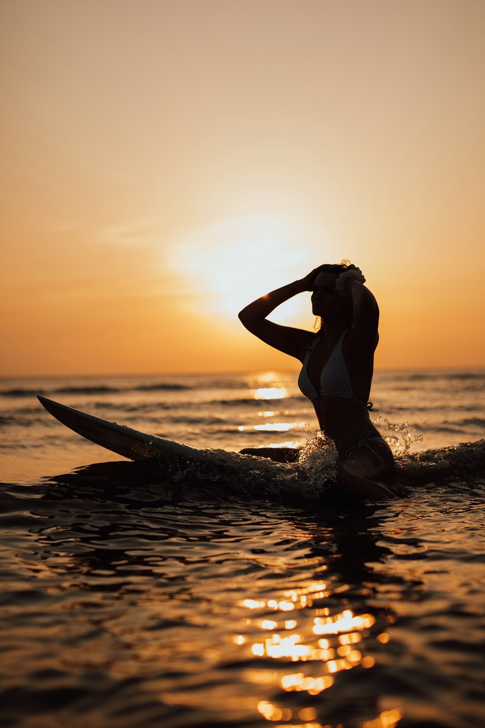 woman in white bikini top and blue denim shorts holding white surfboard on beach during sunset