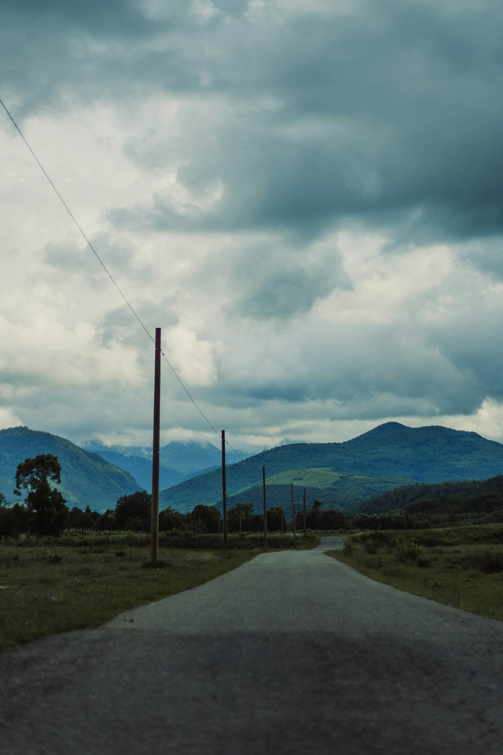 gray concrete road near green grass field and mountain under white clouds during daytime