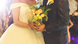 Couple holding hands with white flowers and soft lighting during a vow renewal ceremony.