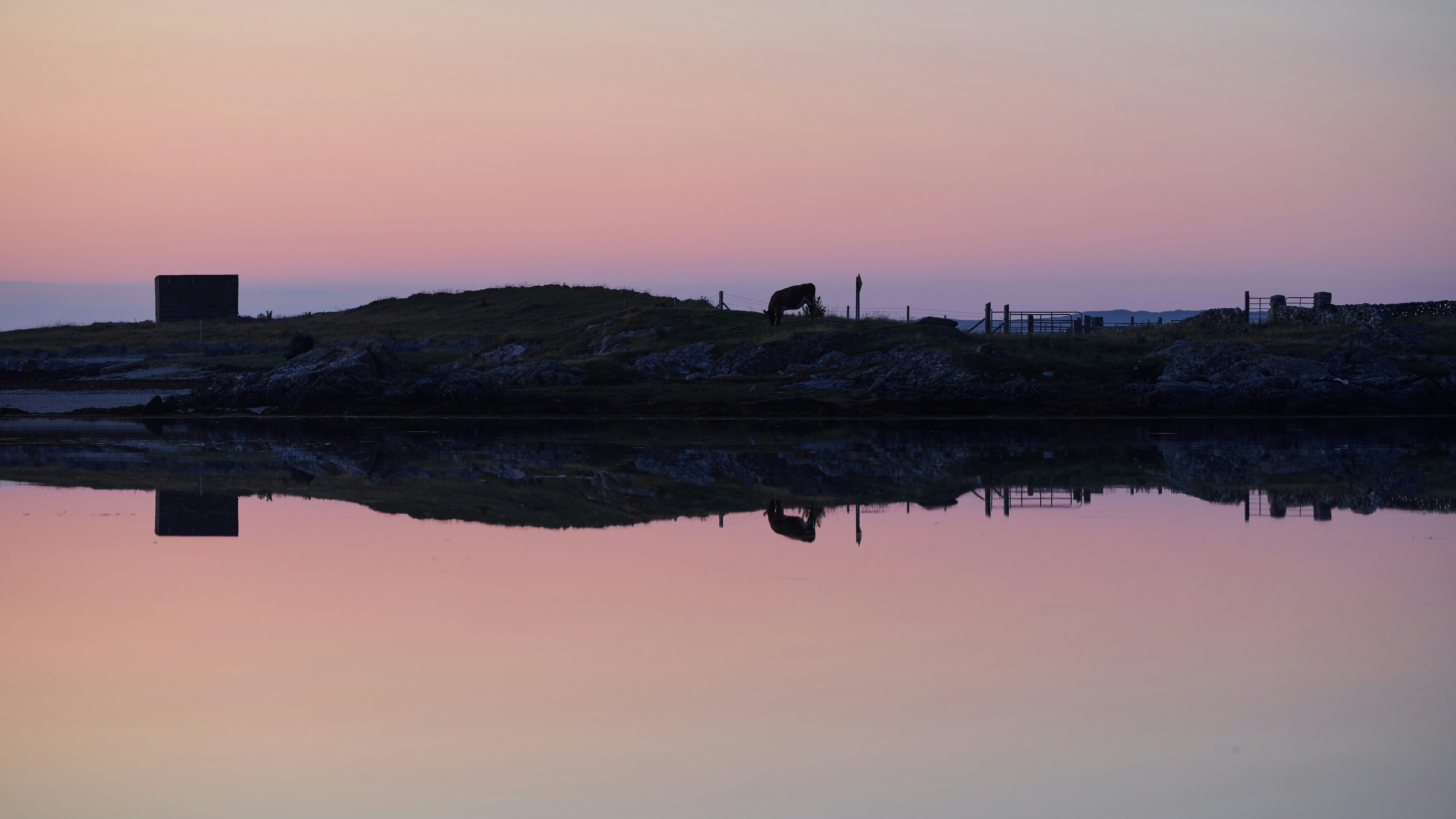 silhouette of person standing on rock formation near body of water during sunset