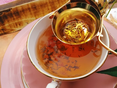 Close-up of deep red and gold tea leaves spilling from a traditional Indian brass container.
