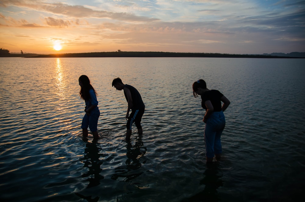 man and woman holding hands while walking on water during sunset