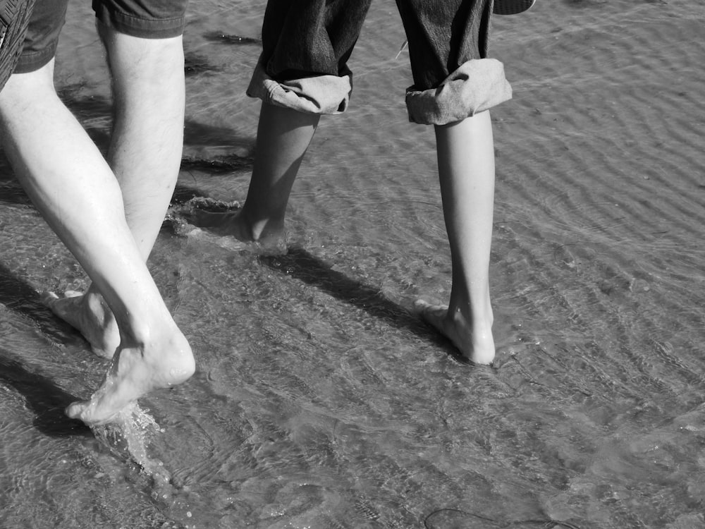 grayscale photo of 2 person standing on sand