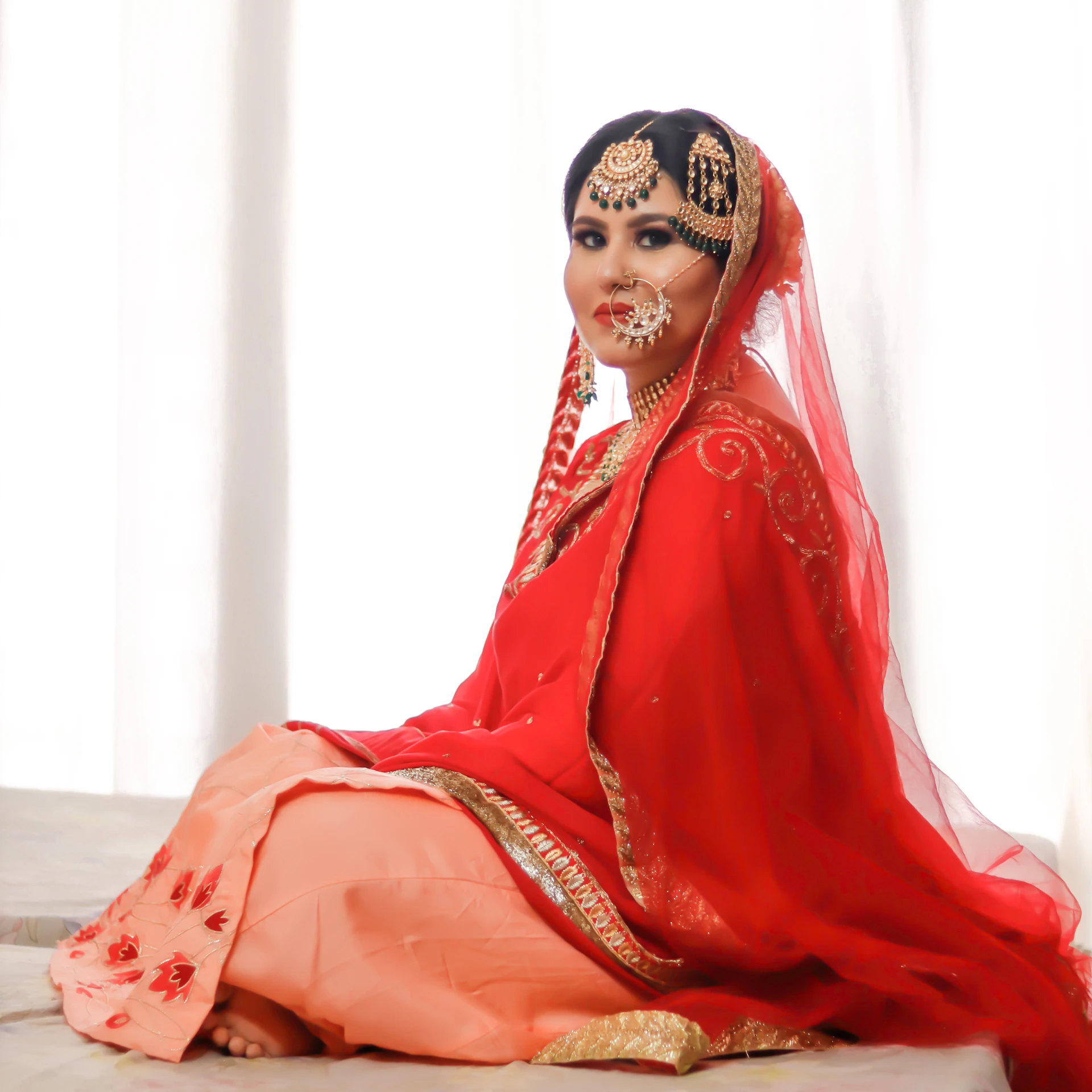 A stunning bridal lehenga in rich red and gold embroidery, displayed on a mannequin with delicate draping and intricate detailing.