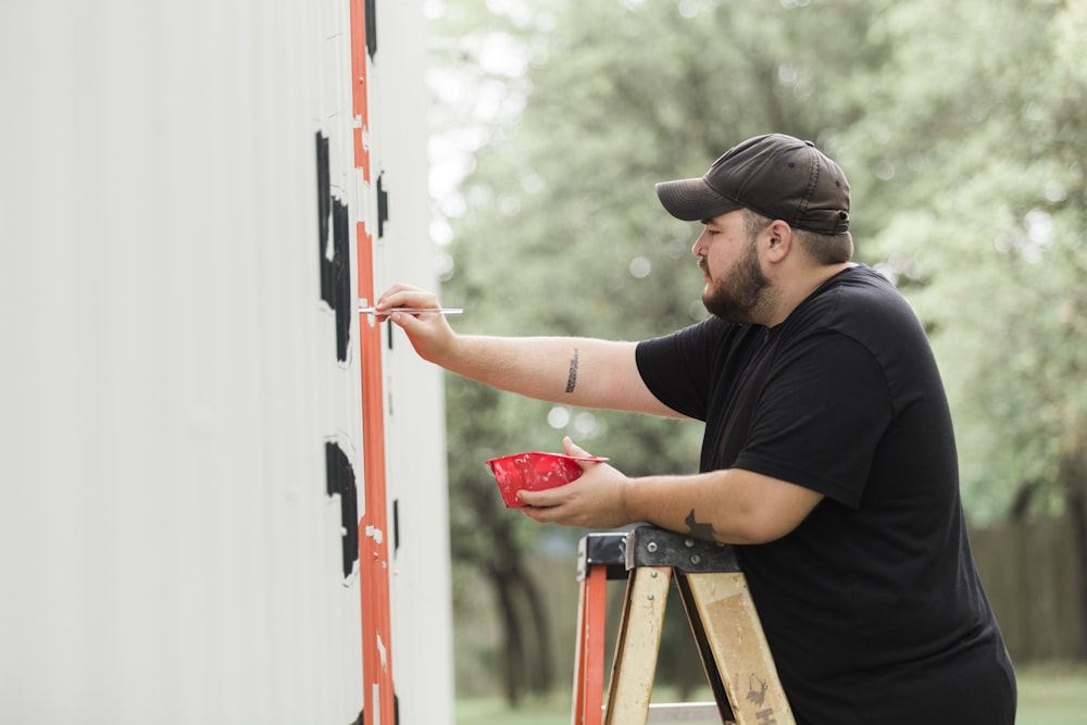 man in black shirt and black cap holding red and white wooden door during daytime