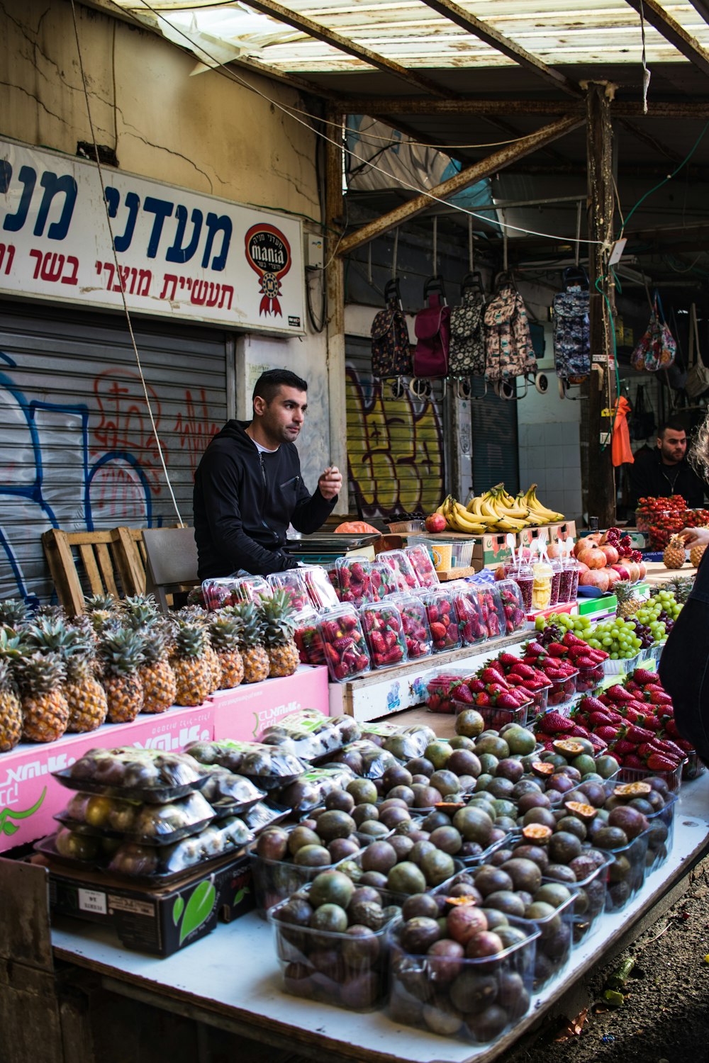 man in black long sleeve shirt standing in front of fruit stand