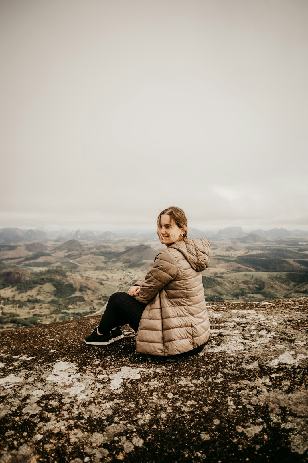 woman in brown coat sitting on rock during daytime