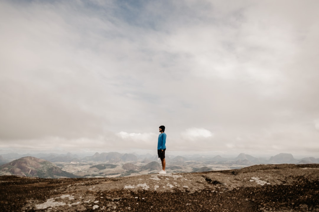 woman in blue shirt and black pants standing on brown rock formation under white clouds during