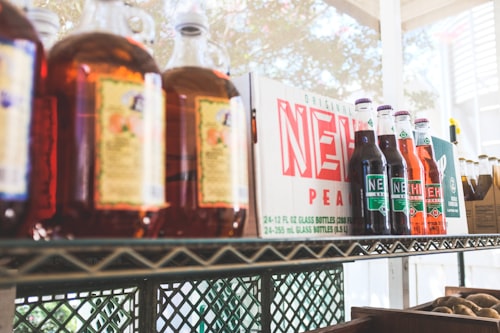 A vintage looking photo of a metal shelving unit with glass soft drinks bottles on it