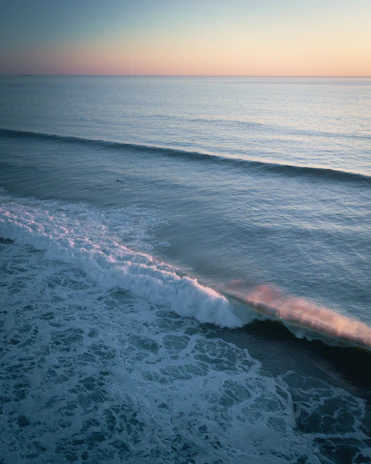 Crisp waves rolling onto a secluded California shore under a soft pastel sunrise.
