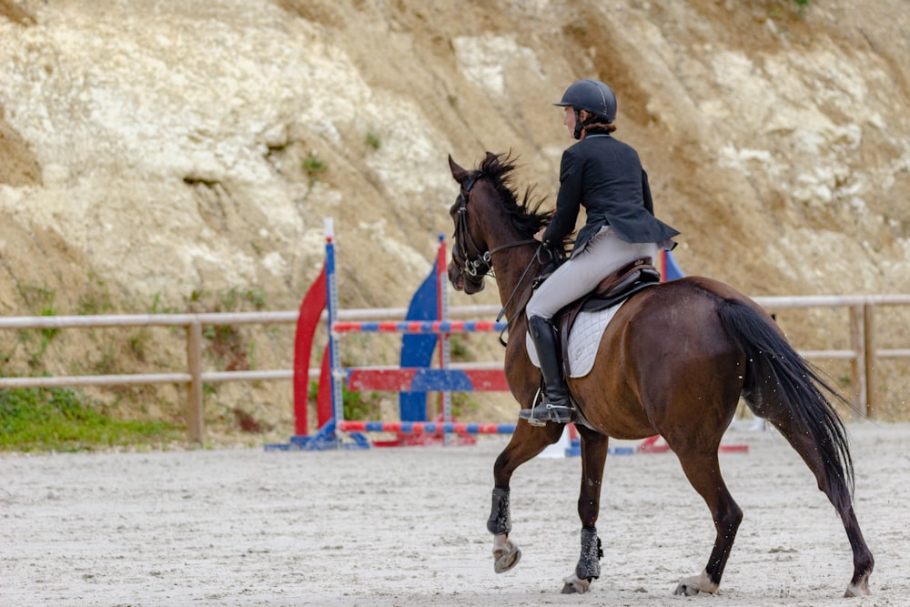 Femme en veste noire chevauchant un cheval brun pendant la journée