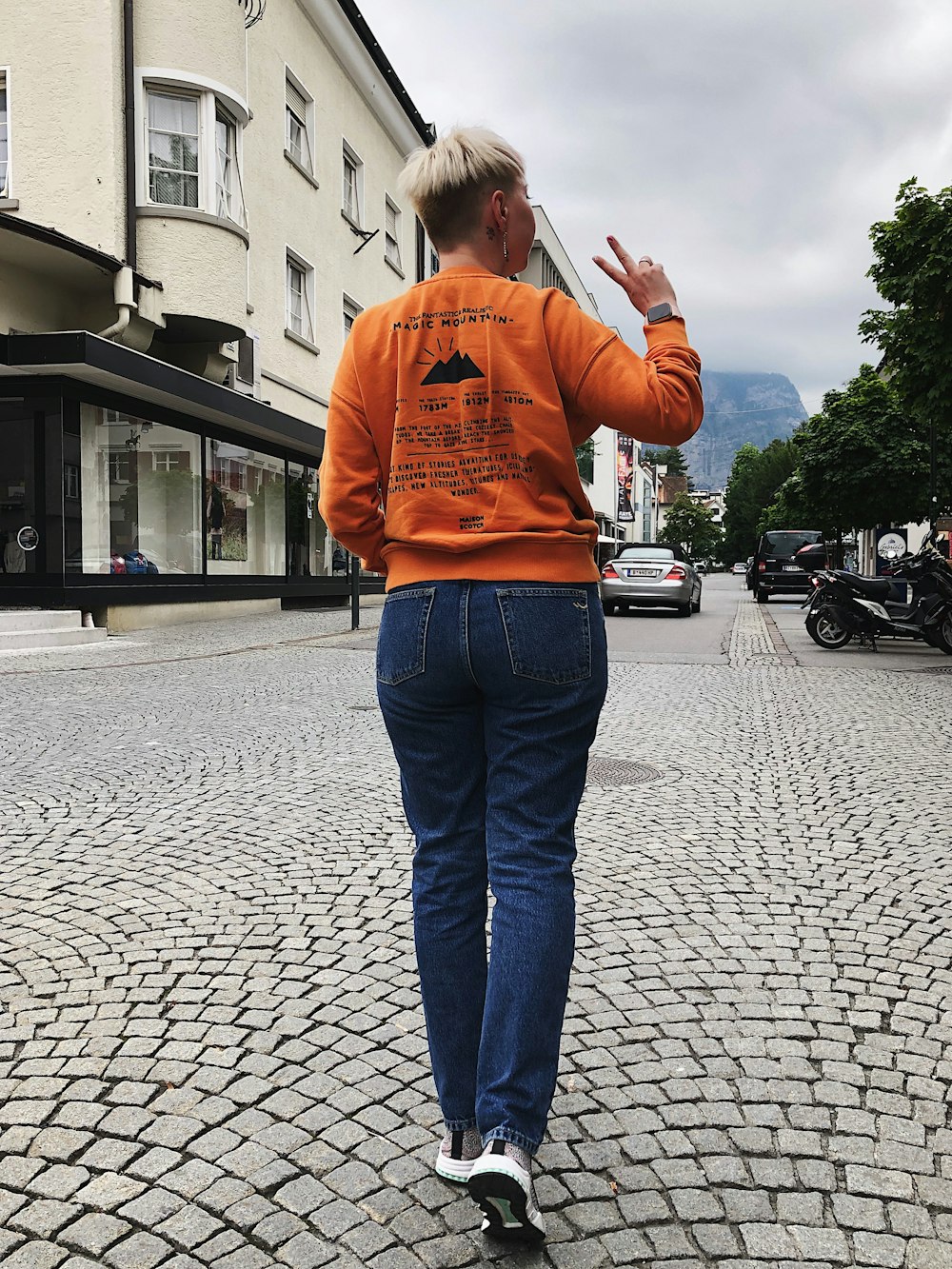woman in orange sweater standing on sidewalk during daytime