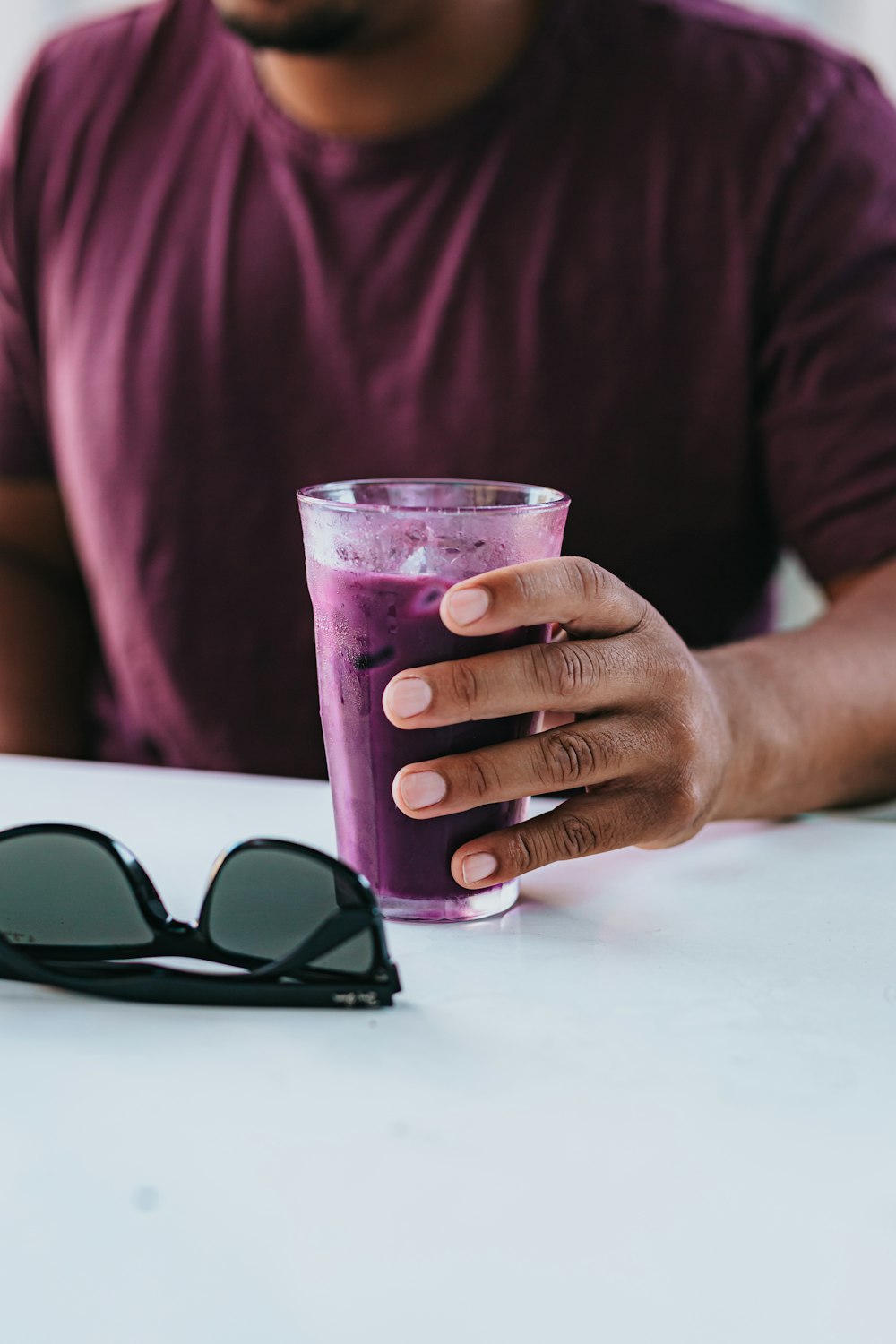 person holding clear drinking glass with black frame sunglasses