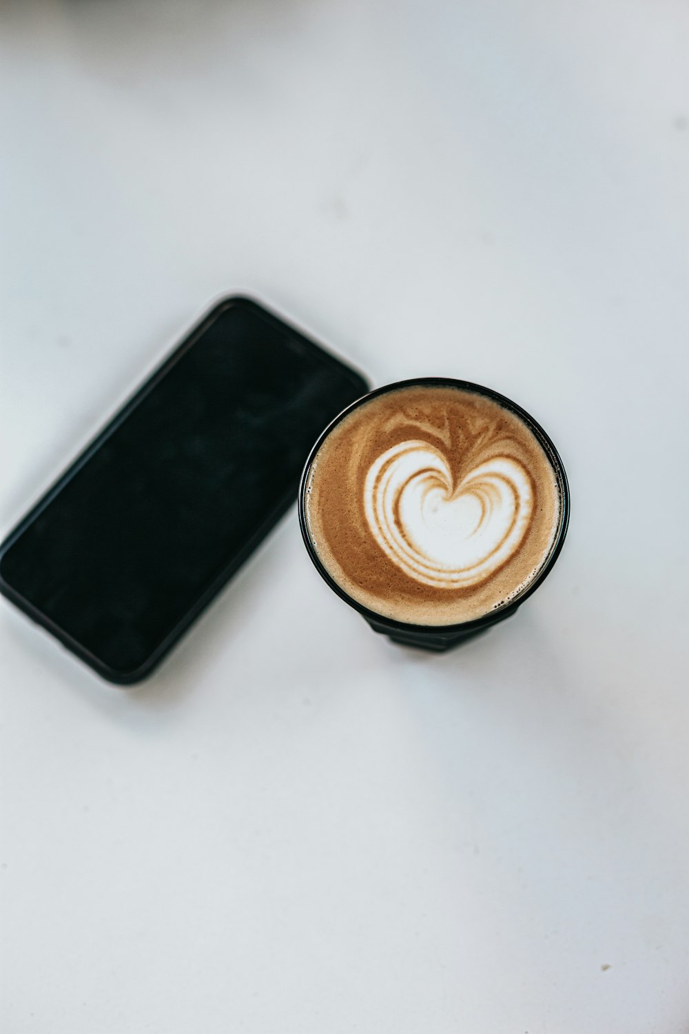 black android smartphone beside brown and white ceramic mug with coffee