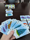 A close-up of colorful playing cards spread out on a wooden table with a child's hand reaching in