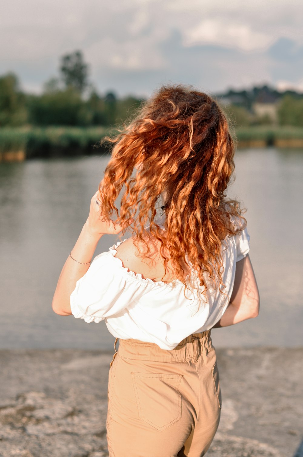 woman in white shirt and brown shorts standing near body of water during daytime