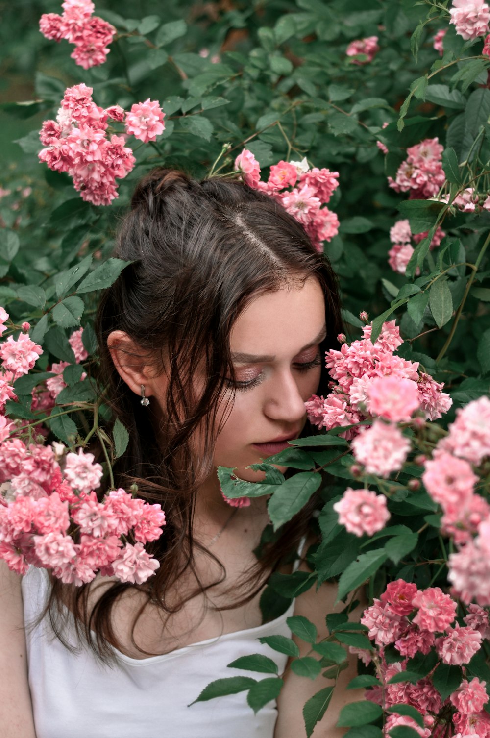 woman in white tank top standing beside pink flowers