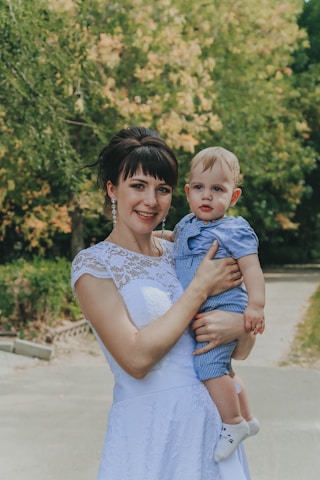 woman in white floral lace sleeveless dress carrying baby in blue and white stripe dress
