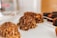 Chocolate-covered confections adorned with nut pieces are arranged in an orderly fashion on a white surface, with a soft background focus.