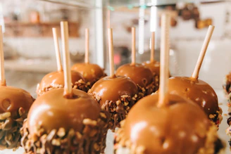 Close-up of a caramel apple dripping with rich caramel, sprinkled with crushed nuts, set against a rustic wooden background.