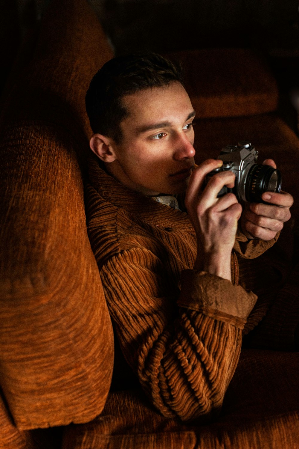 man in brown sweater holding black dslr camera