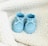A pair of blue baby shoes with white details resting on a fluffy white blanket. The shoes have small white polka dots and lace-up fronts.