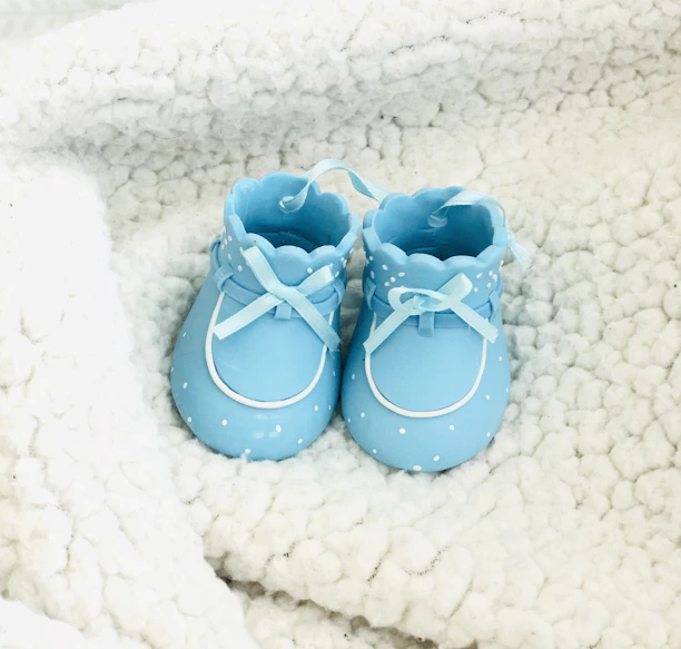 Close-up of tiny baby shoes in mint pastel color on a cream blanket