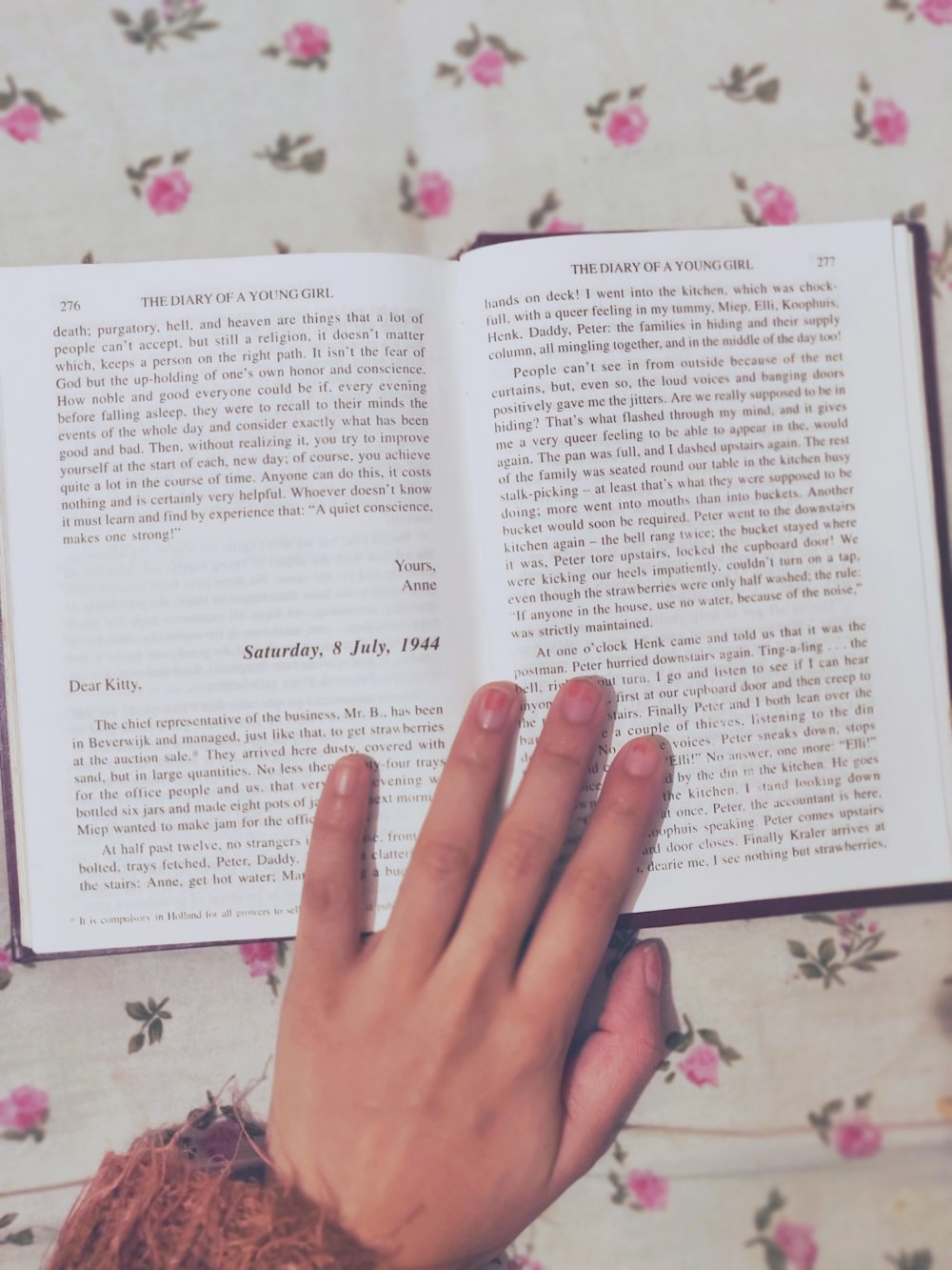 person holding book page on white floral textile