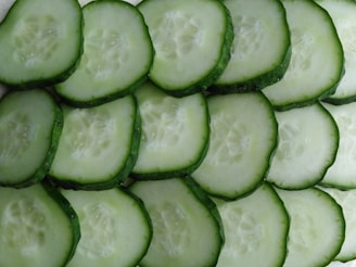Several slices of cucumber are arranged in an overlapping pattern. The cucumber slices show a vibrant green outer skin and a pale, watery interior with visible seeds.